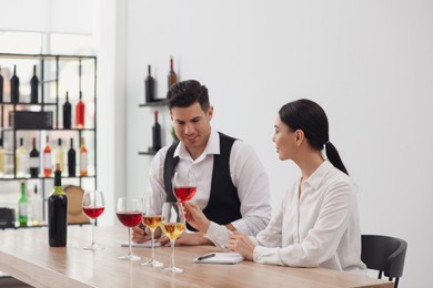 Photo of Sommeliers tasting different sorts of wine at table indoors