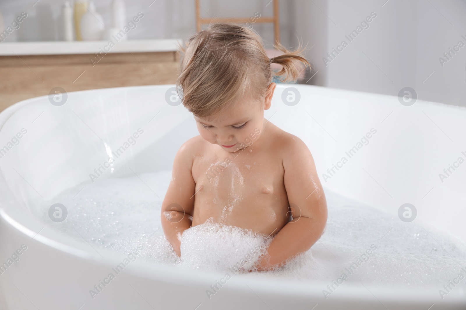 Photo of Cute little girl taking foamy bath at home