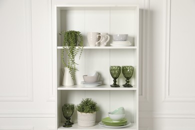 Different clean dishware and houseplants on shelves in cabinet indoors