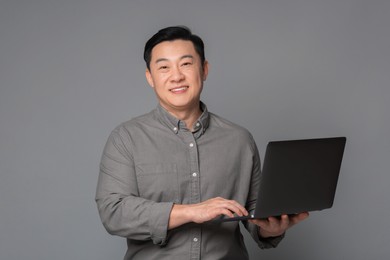 Photo of Portrait of happy businessman with laptop on grey background