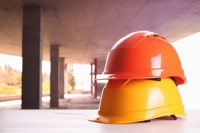 Image of Hard hats on white wooden surface at construction site with unfinished building. Space for text 