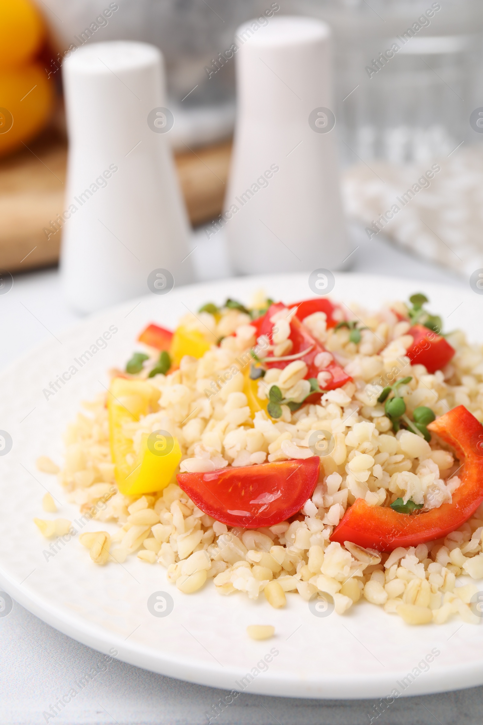 Photo of Plate of cooked bulgur with vegetables on white tiled table, closeup