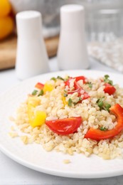 Photo of Plate of cooked bulgur with vegetables on white tiled table, closeup