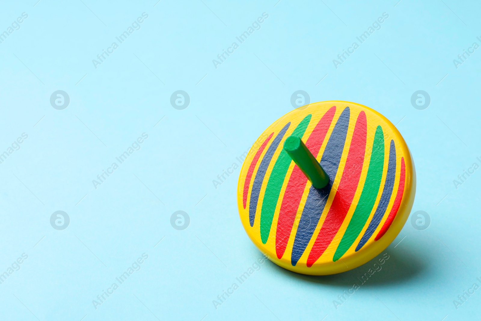 Photo of One colorful spinning top on light blue background, space for text