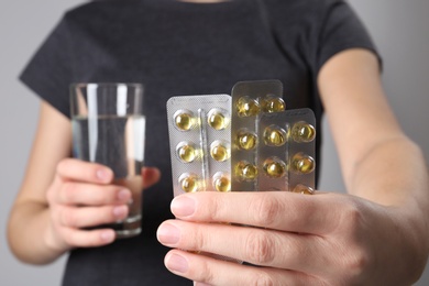 Photo of Woman holding pills in blister packs and glass of water on gray background, closeup