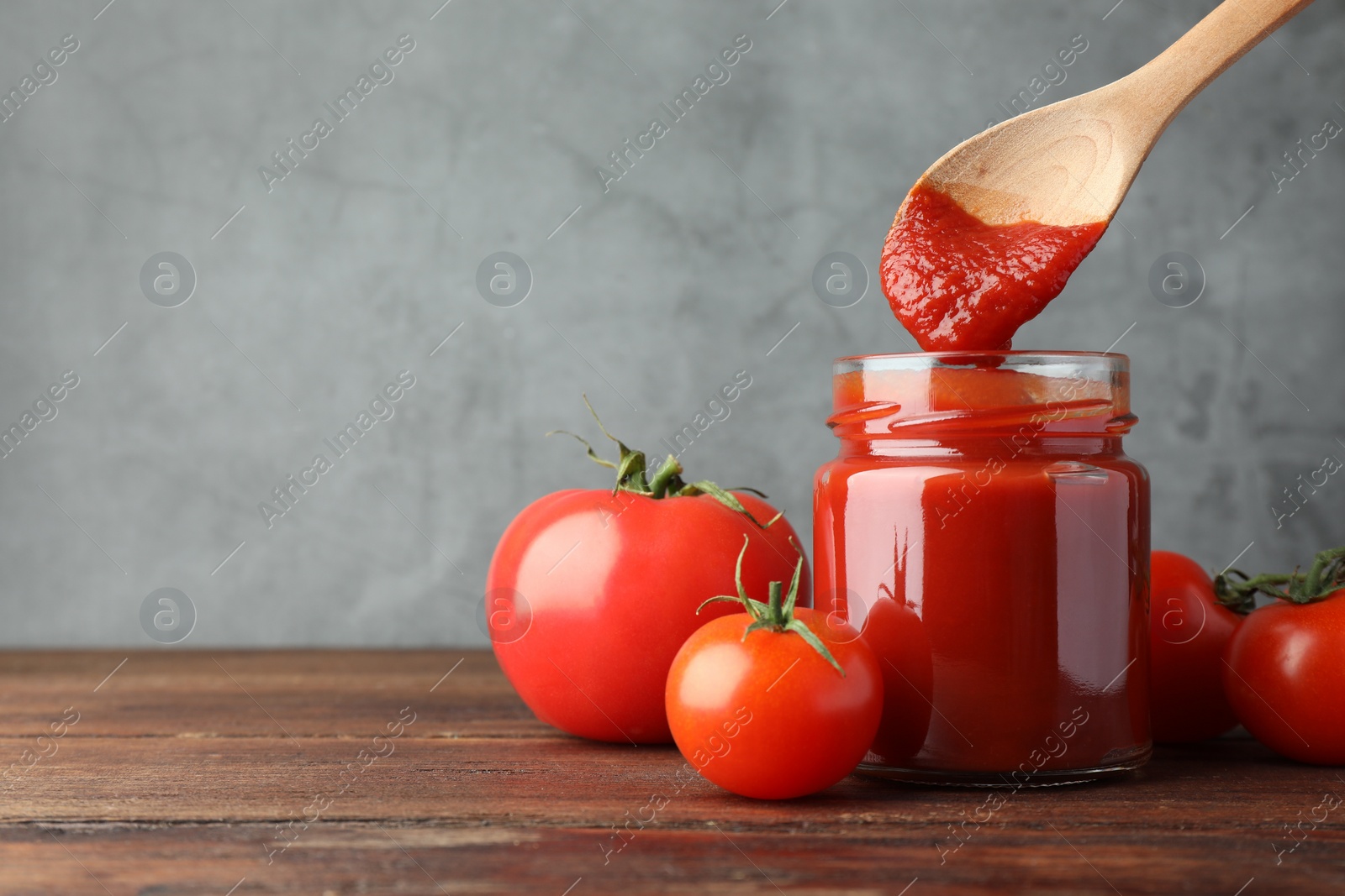 Photo of Taking tasty ketchup with spoon from jar on wooden table, closeup. Space for text