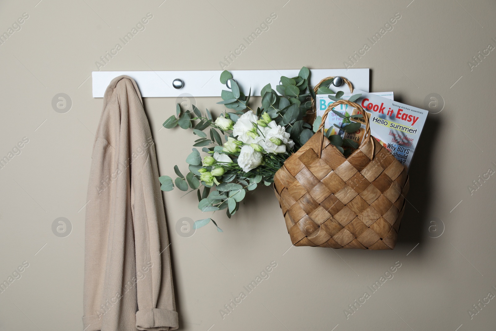 Photo of Stylish straw bag with beautiful bouquet hanging on grey wall