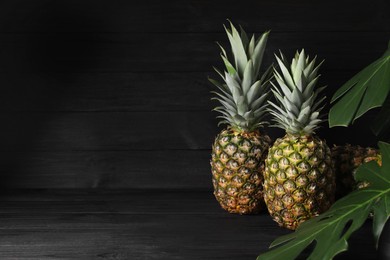 Photo of Whole ripe pineapples on black wooden table, space for text