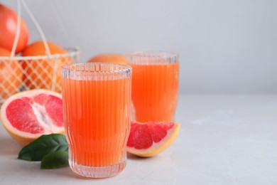 Photo of Tasty freshly made grapefruit juice and fruit on light grey marble table. Space for text