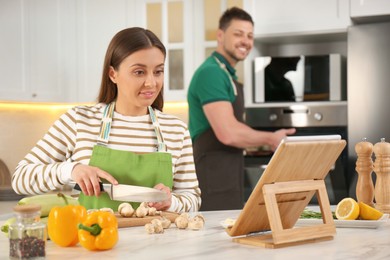 Photo of Couple making dinner together while watching online cooking course via tablet in kitchen
