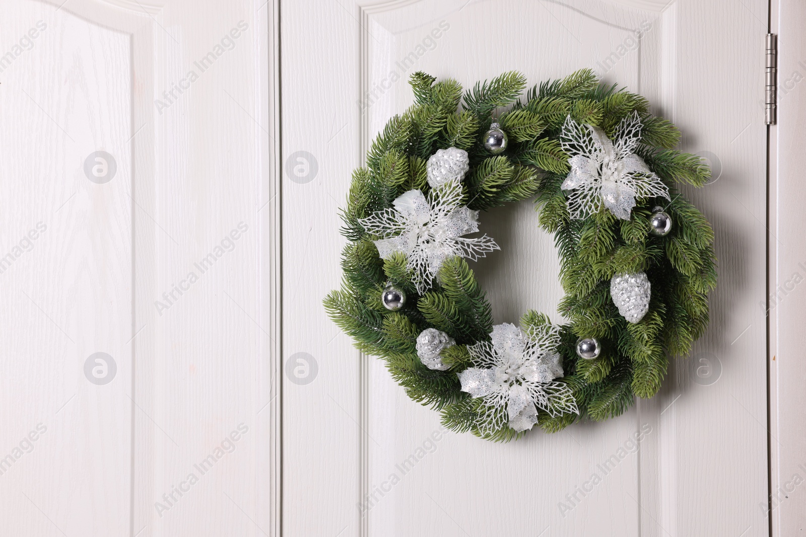 Photo of Beautiful Christmas wreath with festive decor hanging on white door