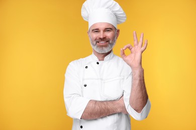 Photo of Happy chef in uniform showing OK gesture on orange background