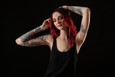 Photo of Beautiful woman with tattoos on arms against black background