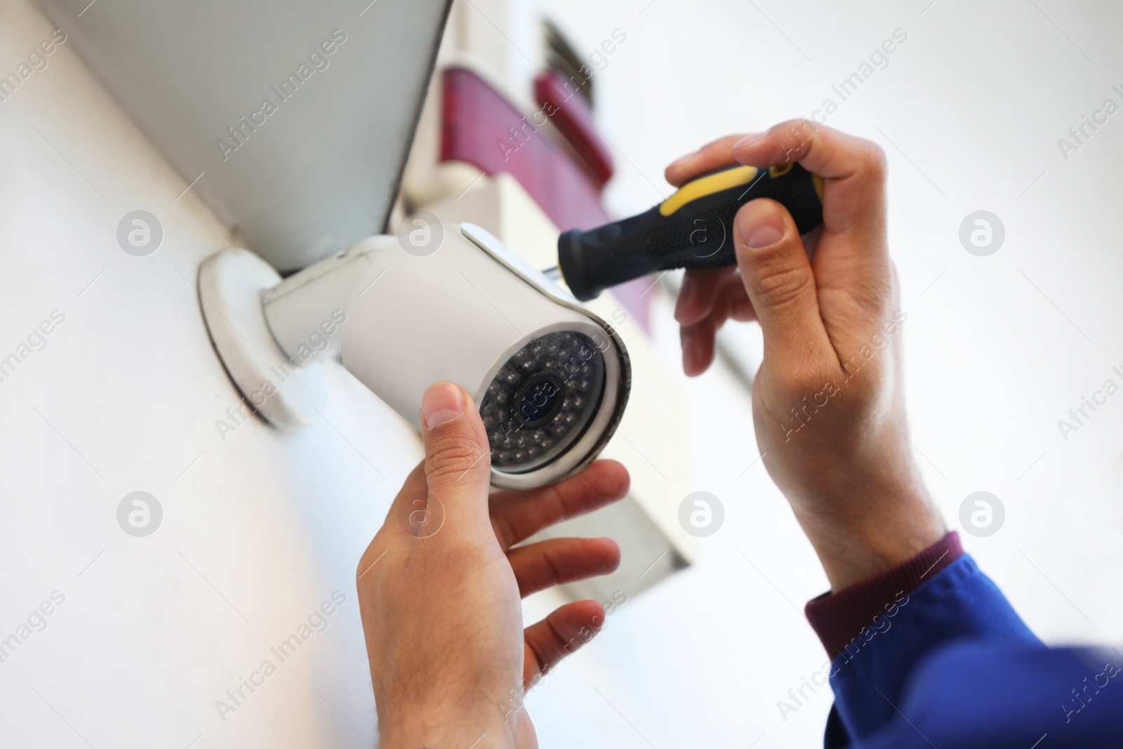 Photo of Technician installing CCTV camera on wall outdoors, closeup