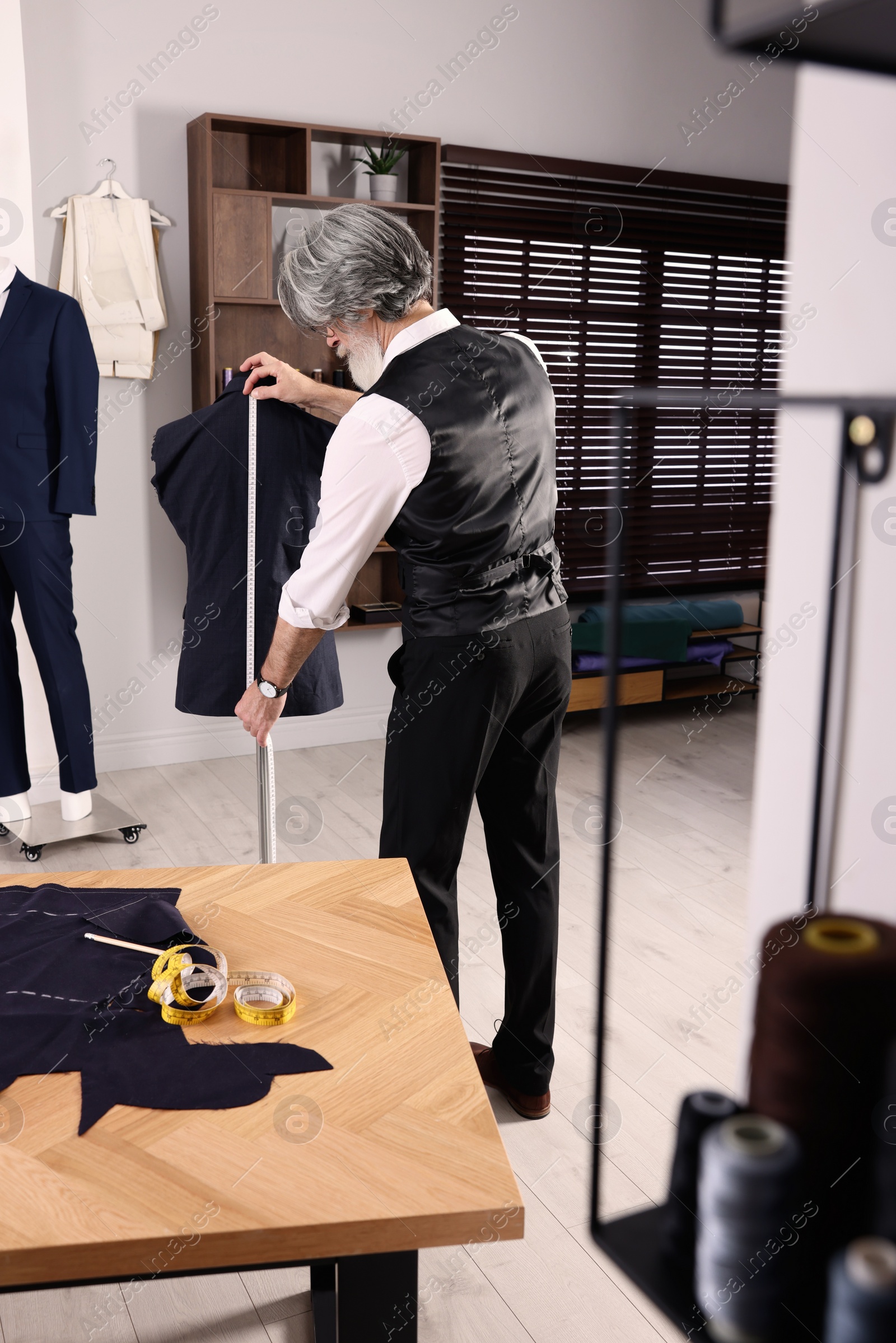Photo of Professional tailor with measuring tape working in atelier