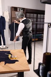 Photo of Professional tailor with measuring tape working in atelier