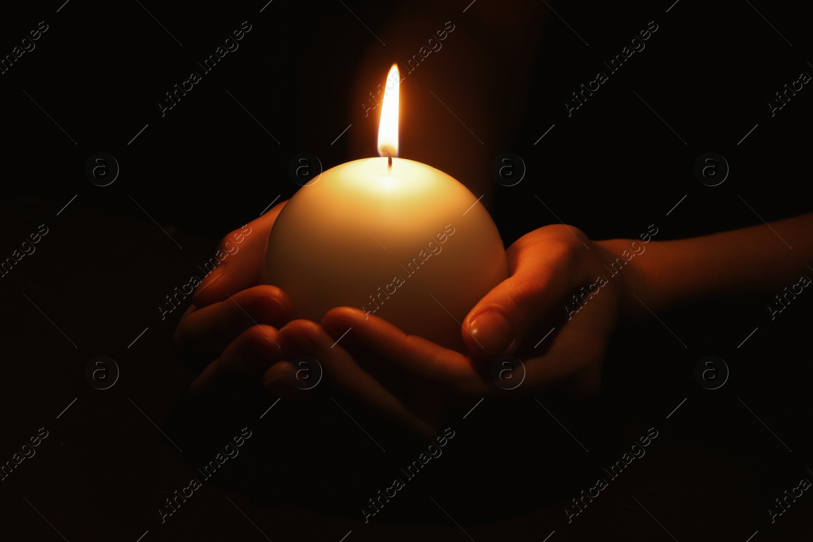 Photo of Woman holding burning candle in hands on black background, closeup