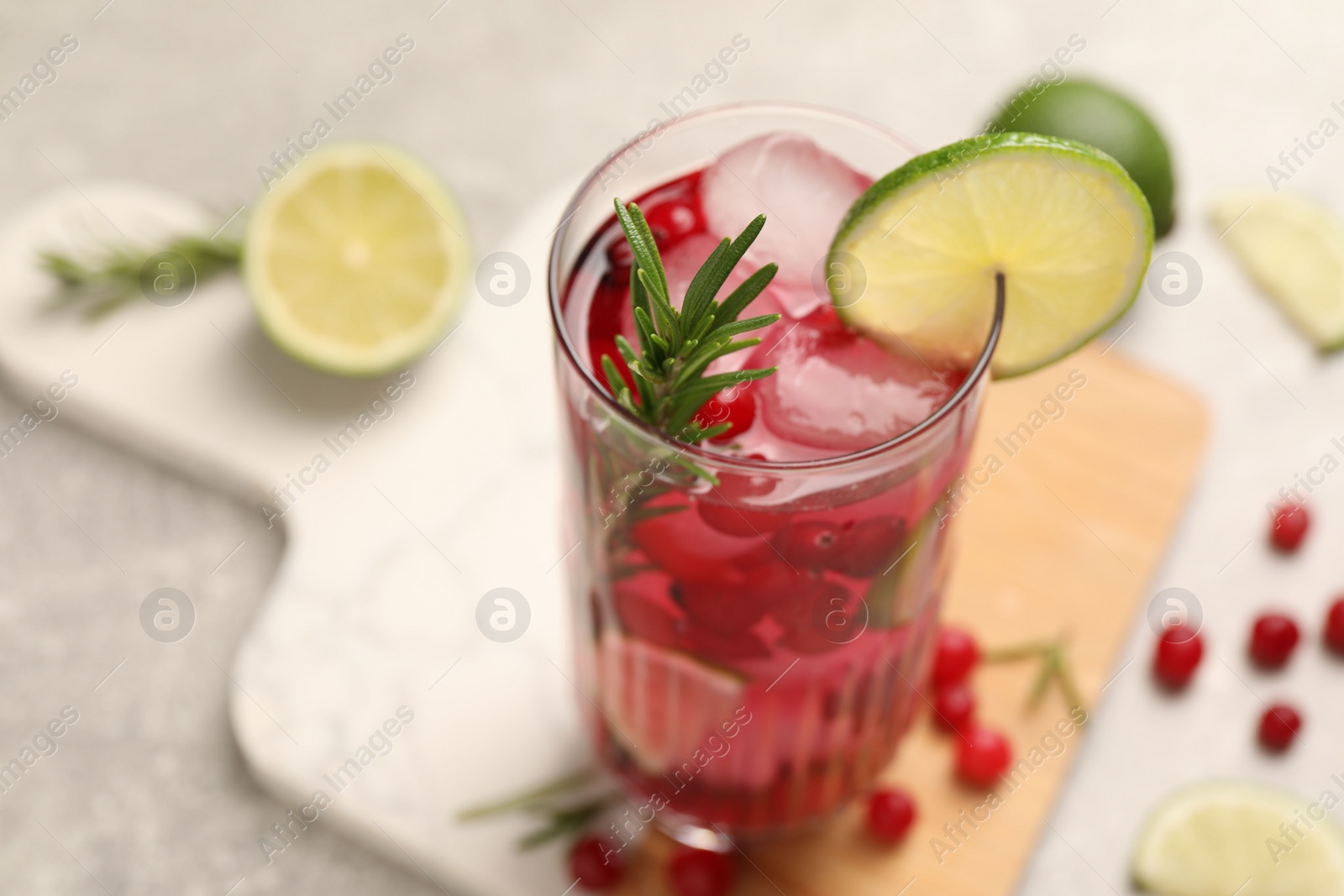 Photo of Tasty cranberry cocktail with rosemary and lime in glass on table, closeup. Space for text