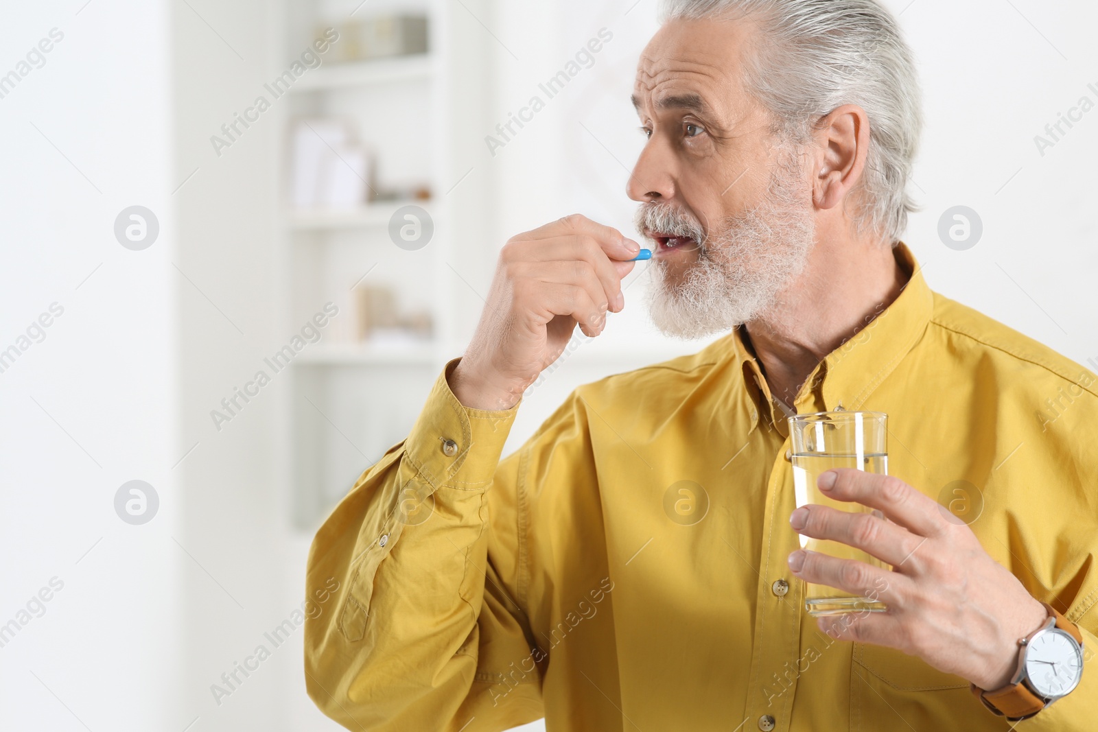 Photo of Senior man with glass of water taking pill indoors. Space for text