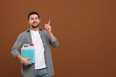 Photo of Man holding canister with blue liquid and pointing at something on brown background. Space for text