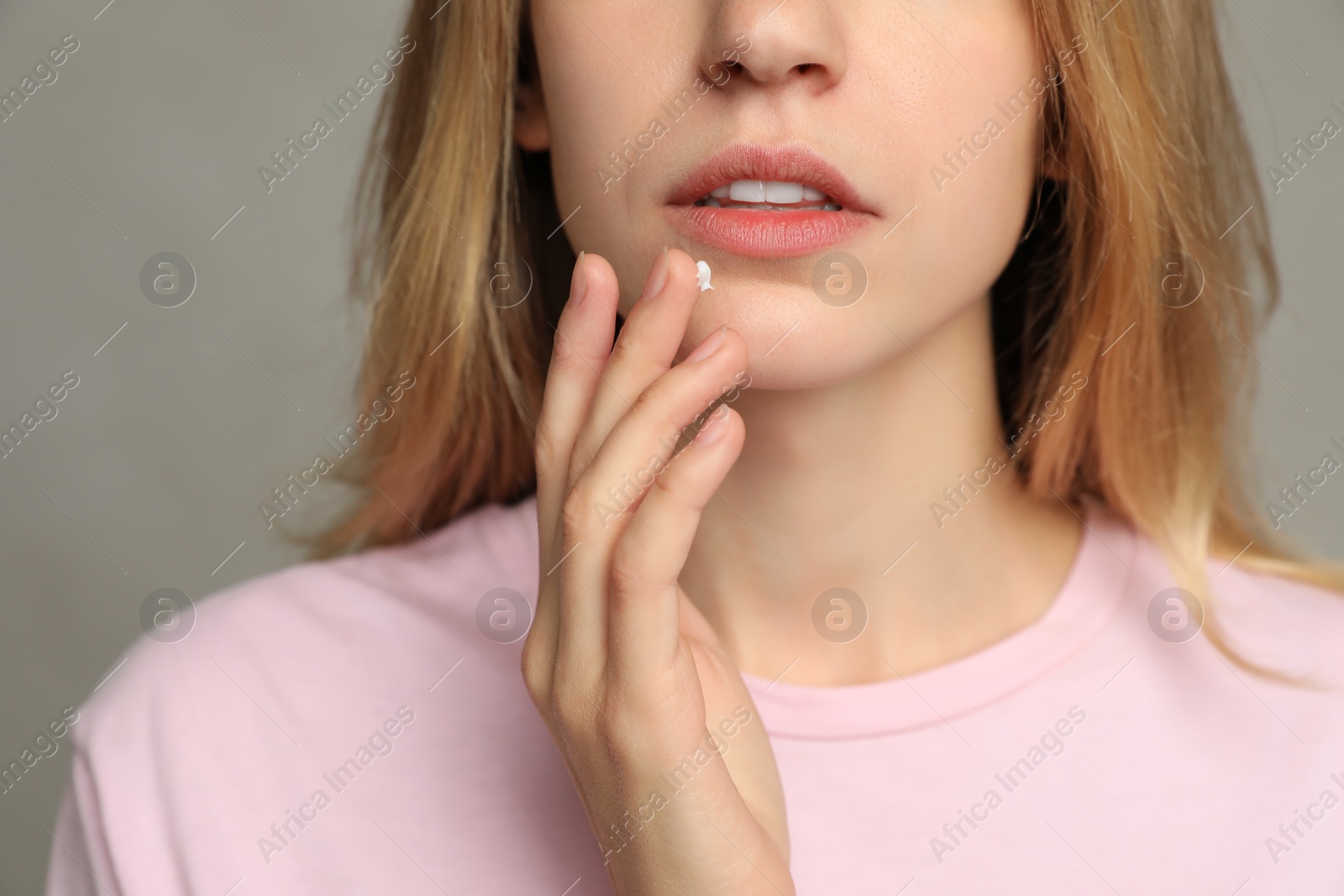 Photo of Woman with herpes applying cream onto lip against light grey background, closeup