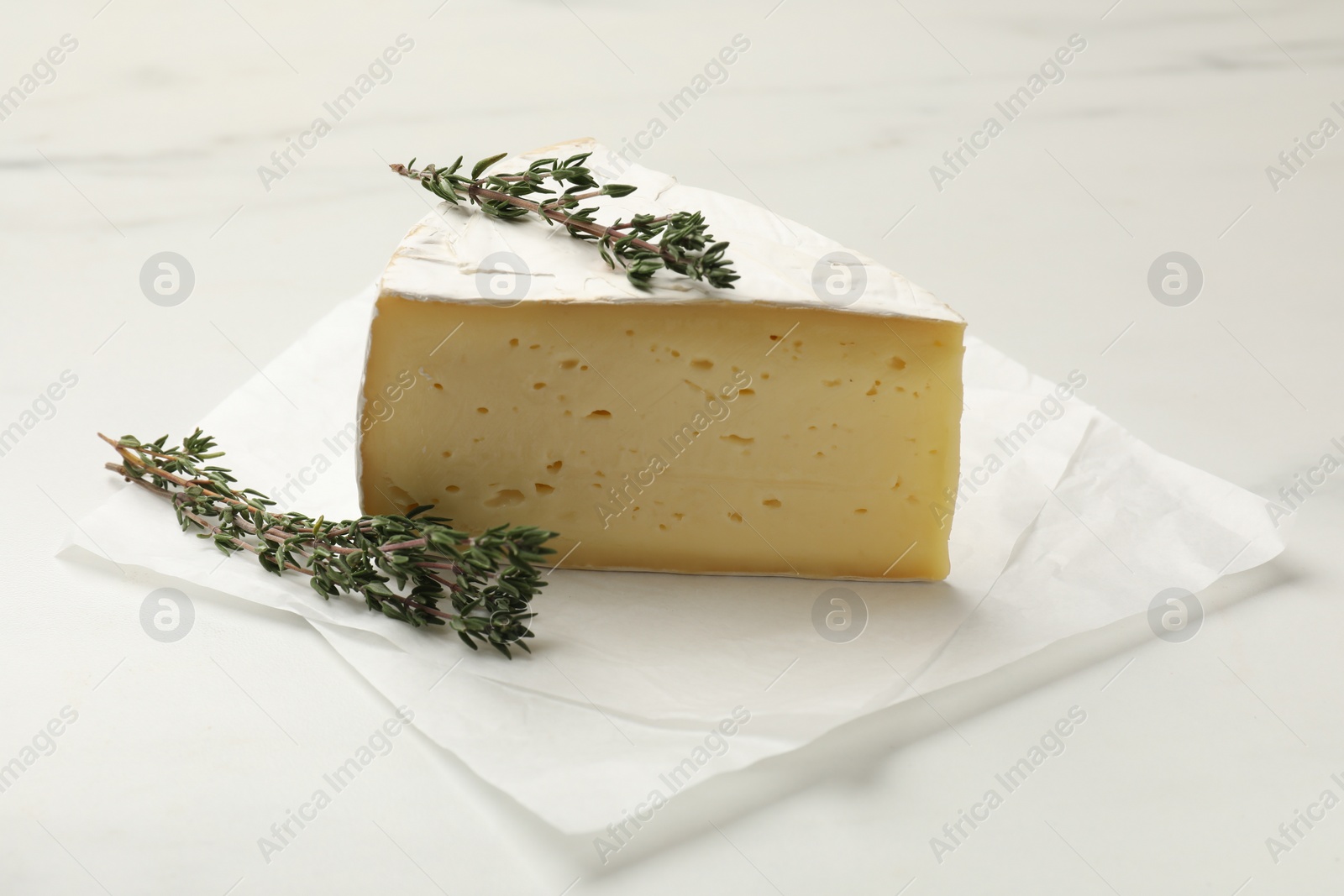 Photo of Piece of tasty camembert cheese and thyme on white table, closeup