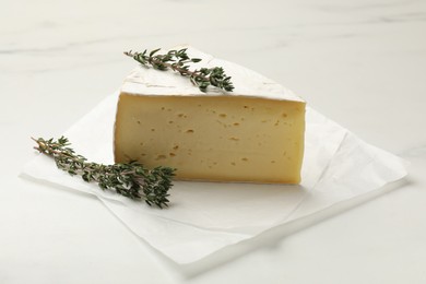 Piece of tasty camembert cheese and thyme on white table, closeup