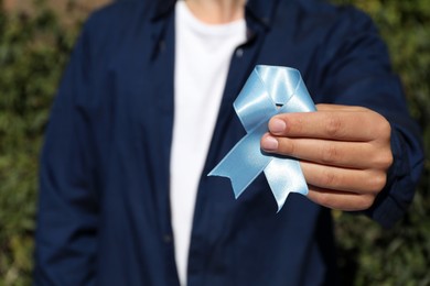 Photo of Man holding light blue ribbon outdoors, closeup. World Diabetes Day