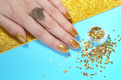 Woman showing manicured hand with golden nail polish and glitter on color background, closeup