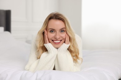 Photo of Happy woman in stylish warm sweater lying on bed indoors