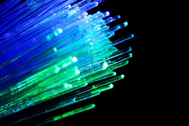 Image of Optical fiber strands transmitting green and blue light on black background, macro view