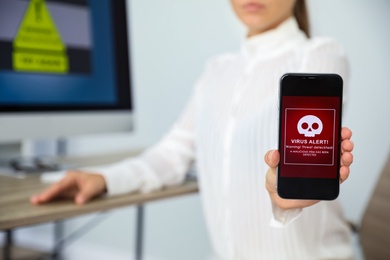 Photo of Woman holding smartphone with warning about virus attack in office, closeup. Space for text