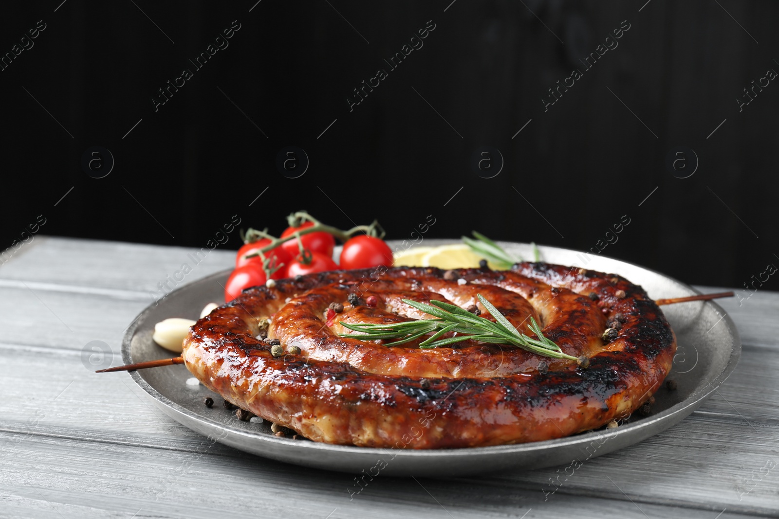 Photo of Delicious homemade sausage with spices, tomatoes and lemon on light grey wooden table against black background, closeup