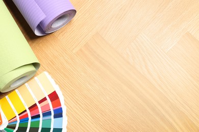 Photo of Different wallpaper rolls and color palette samples on wooden table, flat lay. Space for text