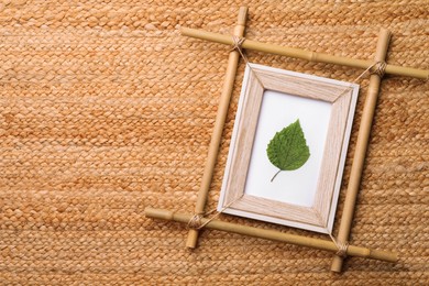 Photo of Bamboo frame with green leaf on wicker straw background, top view. Space for text