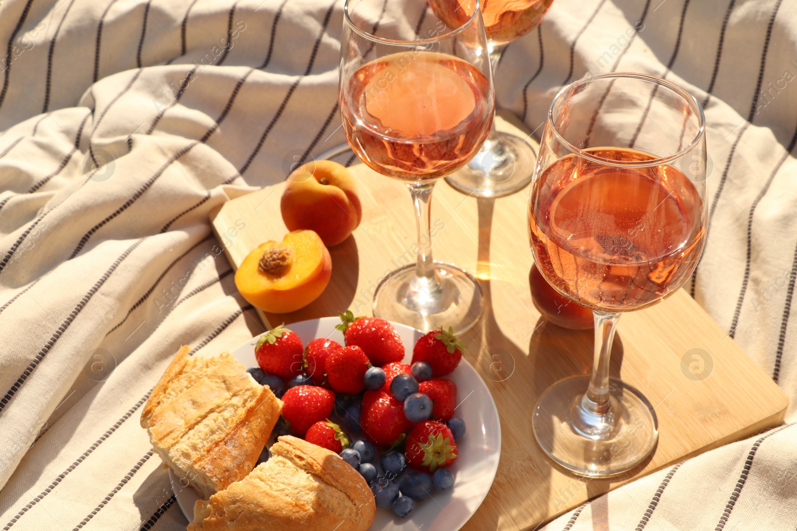 Photo of Glasses of delicious rose wine and food on white picnic blanket