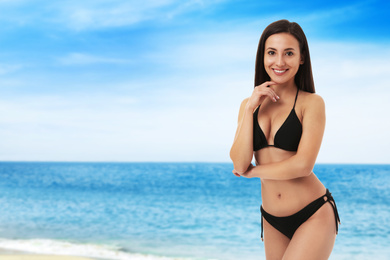 Image of Pretty sexy woman with slim body in stylish black bikini near ocean on sunny day, space for text