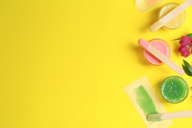 Flat lay composition with different types of wax and spatulas on yellow background. Space for text