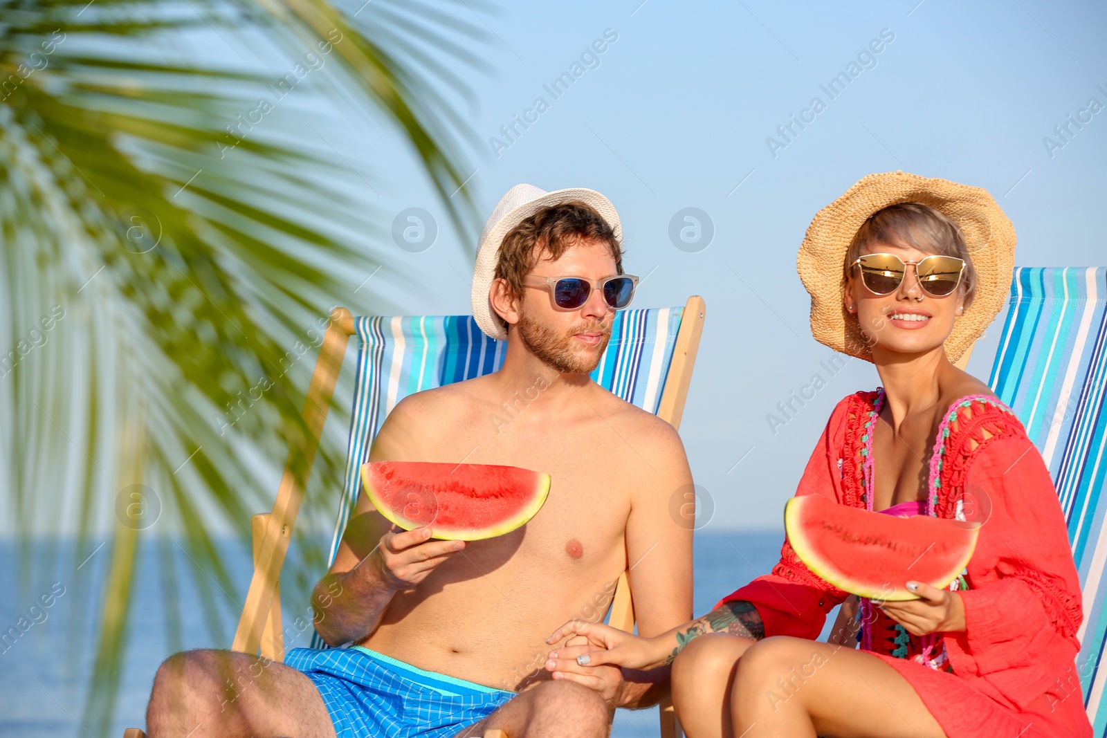 Photo of Young couple with watermelon slices in beach chairs at seacoast