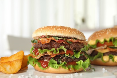 Tasty burgers with bacon and fried potatoes on table