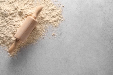 Photo of Pile of flour and rolling pin on light textured table, top view. Space for text
