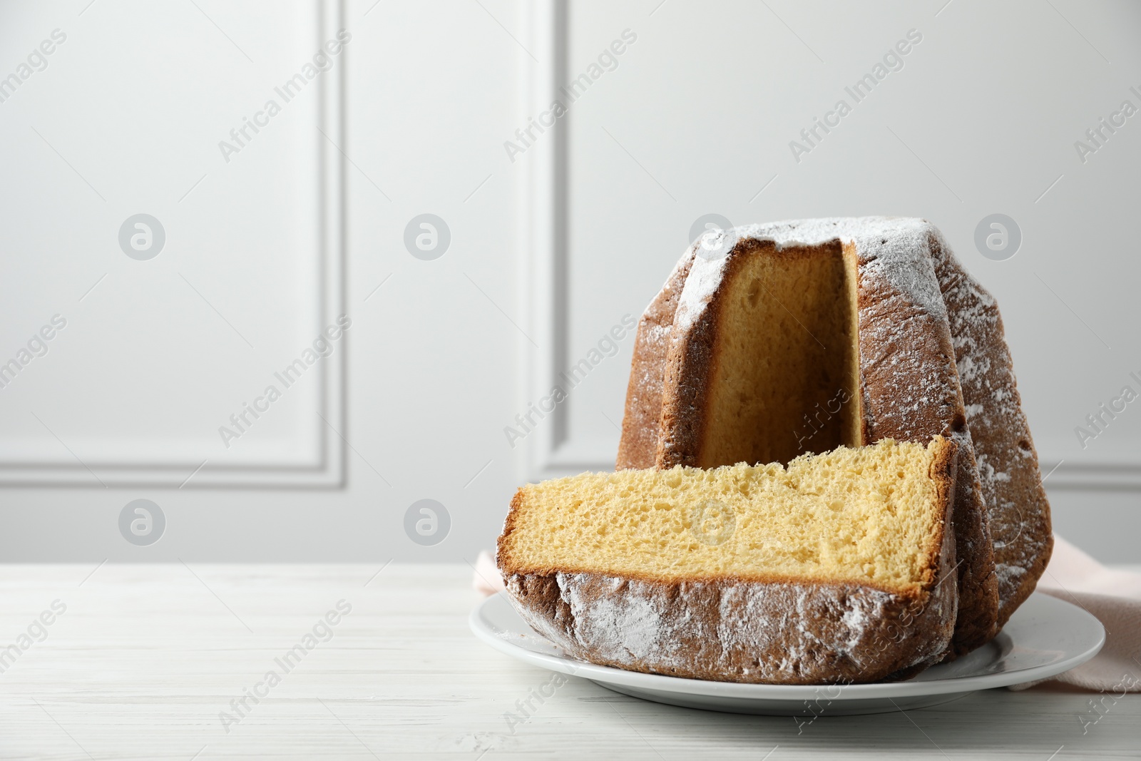 Photo of Delicious Pandoro cake decorated with powdered sugar on white wooden table, space for text. Traditional Italian pastry