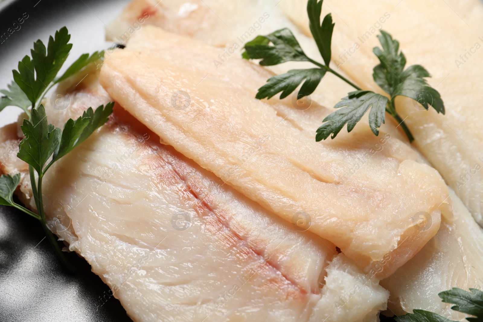 Photo of Raw cod fish and parsley on plate, closeup