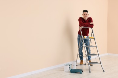 Photo of Young handsome man near metal stepladder and painting tools indoors, space for text. Room renovation