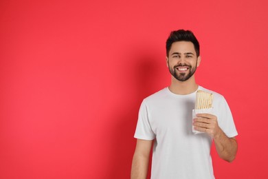 Happy young man holding tasty shawarma on red background. Space for text