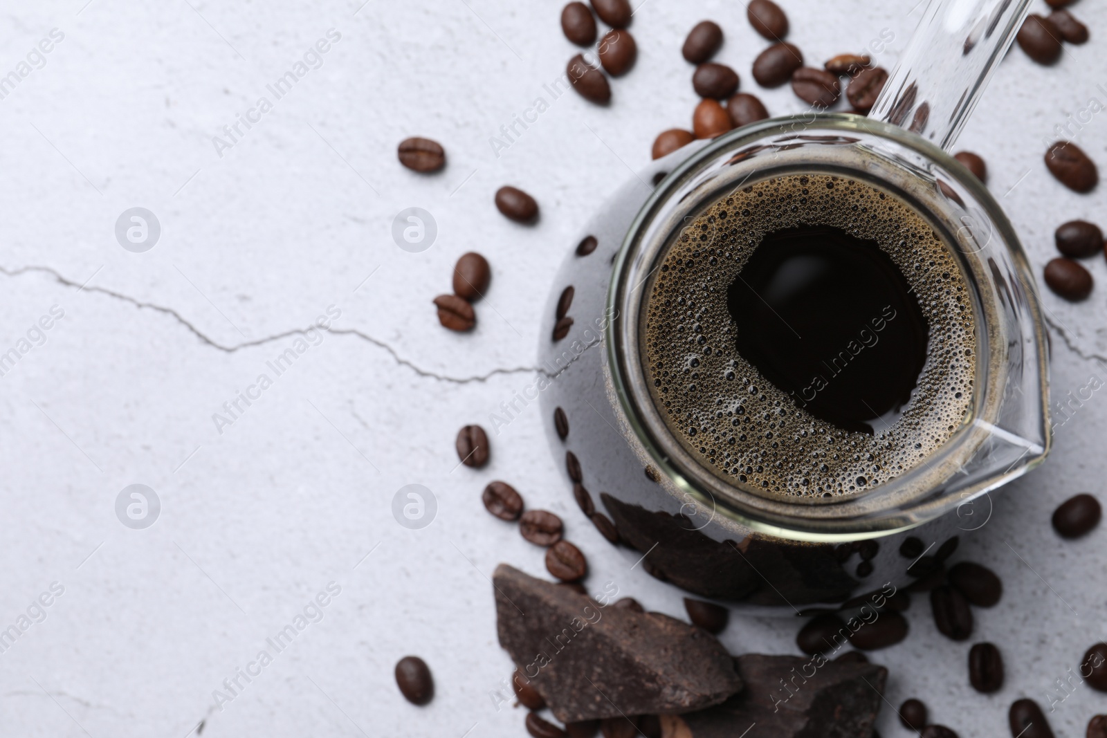 Photo of Turkish coffee in glass cezve, beans and chocolate on light grey table, flat lay. Space for text