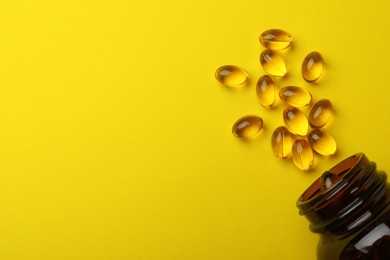 Photo of Overturned bottle with dietary supplement capsules on yellow background, flat lay. Space for text