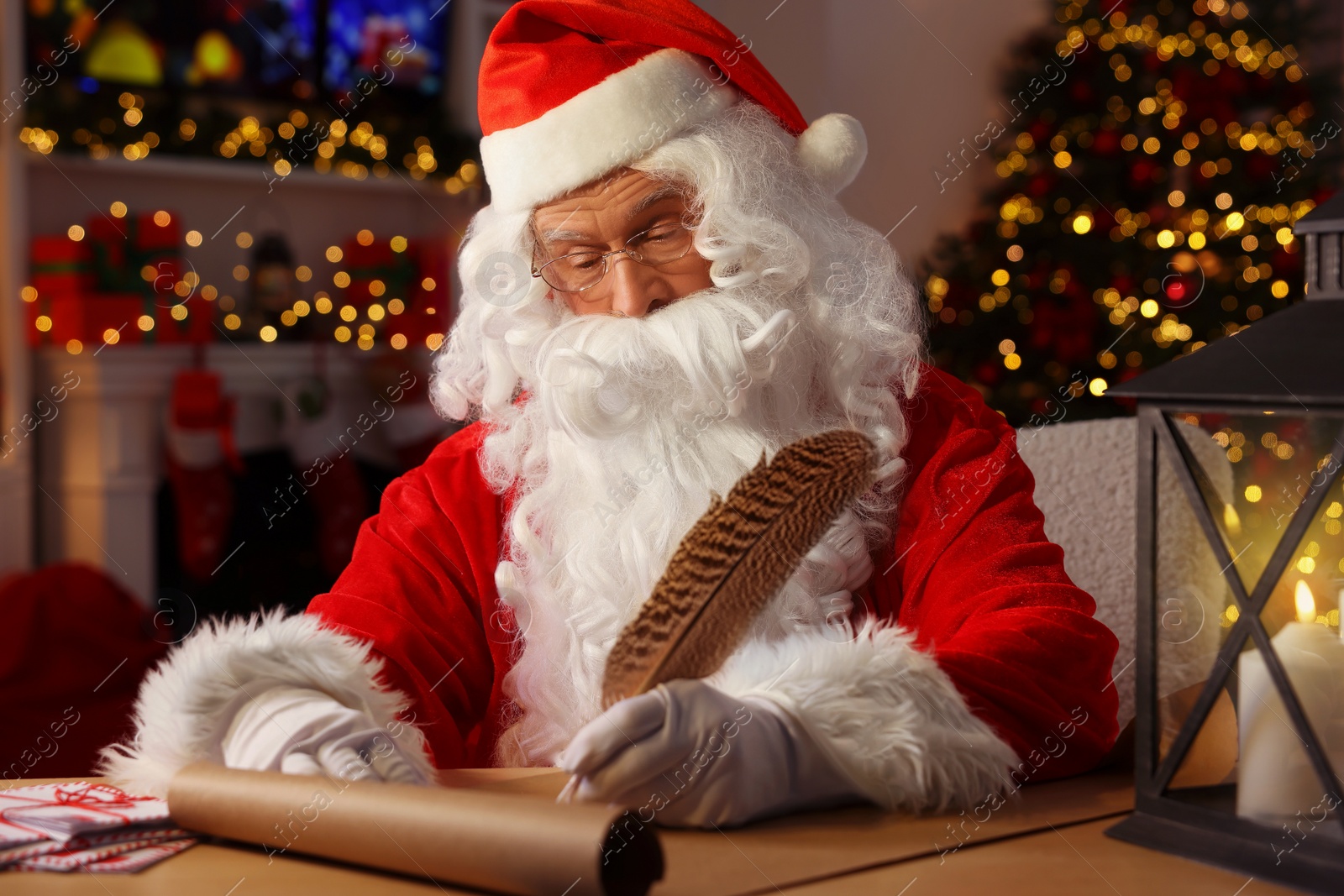 Photo of Santa Claus writing letter at table in room decorated for Christmas