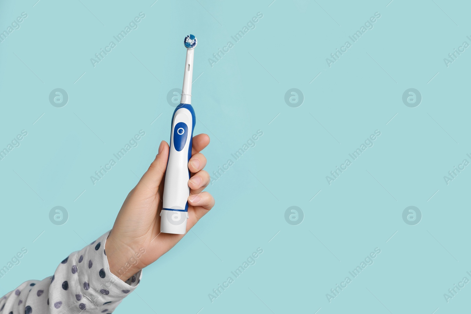 Photo of Woman holding electric toothbrush on light blue background, closeup. Space for text