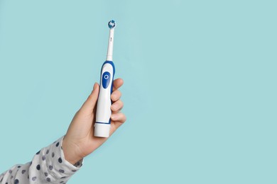 Photo of Woman holding electric toothbrush on light blue background, closeup. Space for text